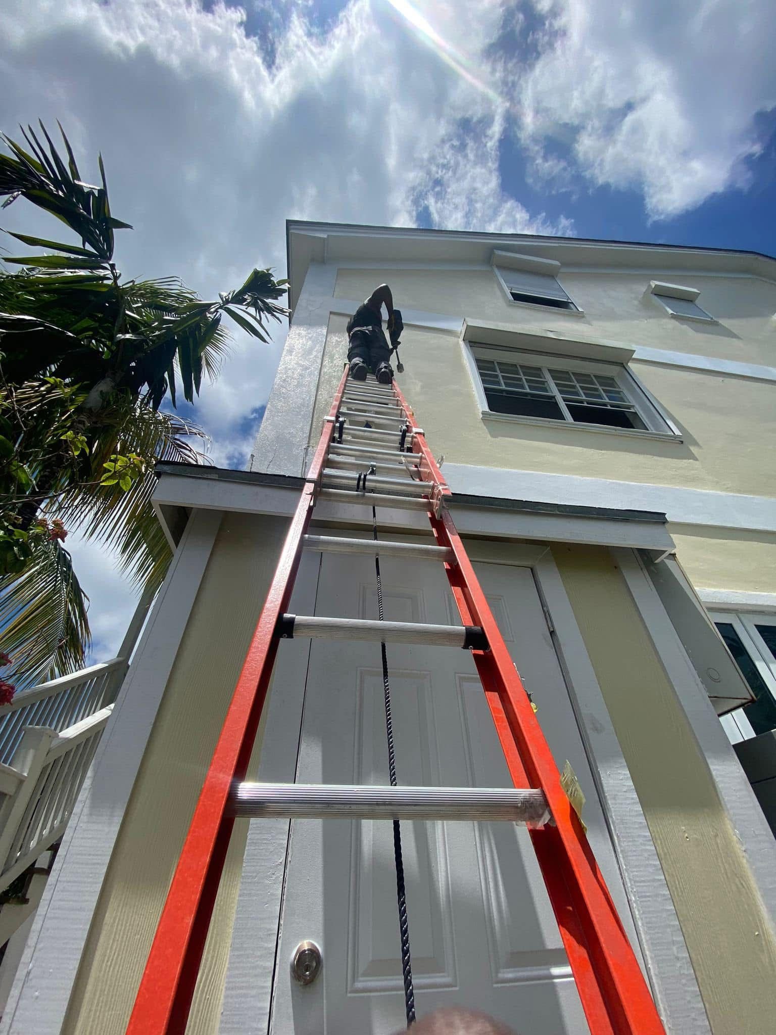 Technician climbing tall ladder on Nassau residential building