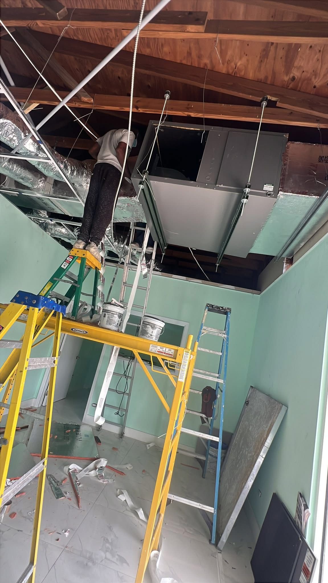 Technician installing AC unit in commercial space with scaffolding