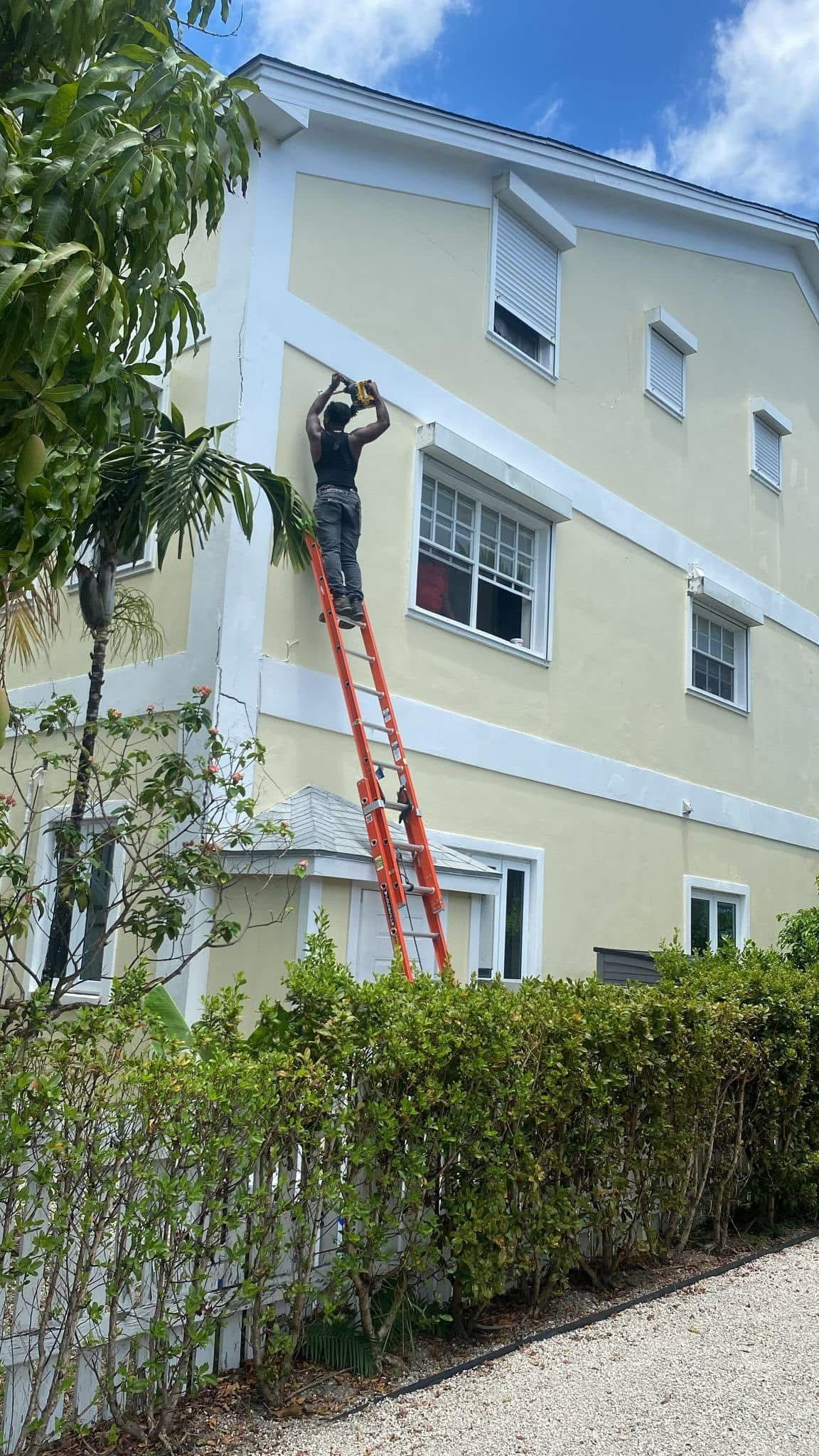 Technician on ladder installing AC on multi-storey Nassau home