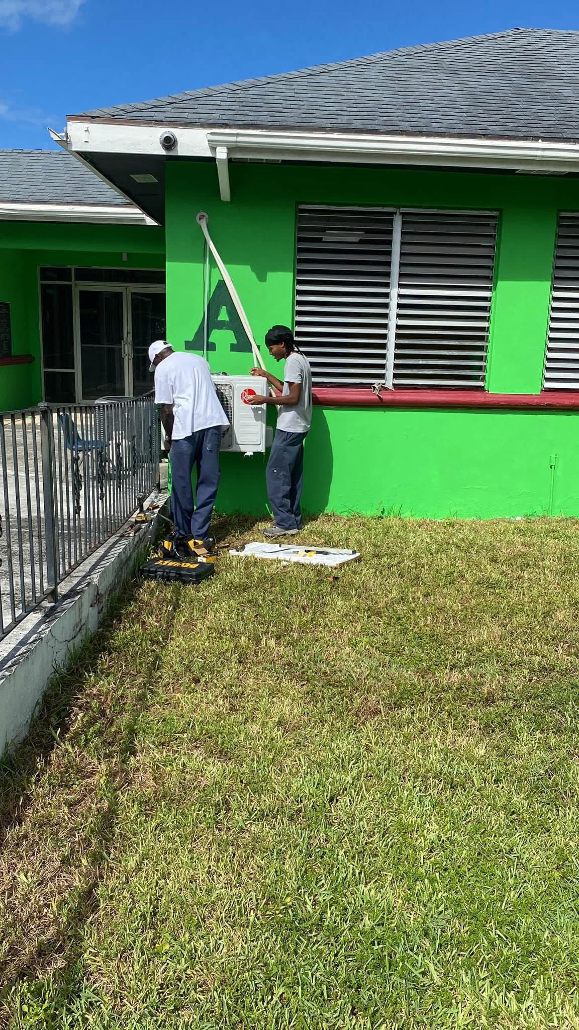 Two technicians installing Rheem AC unit on green building exterior