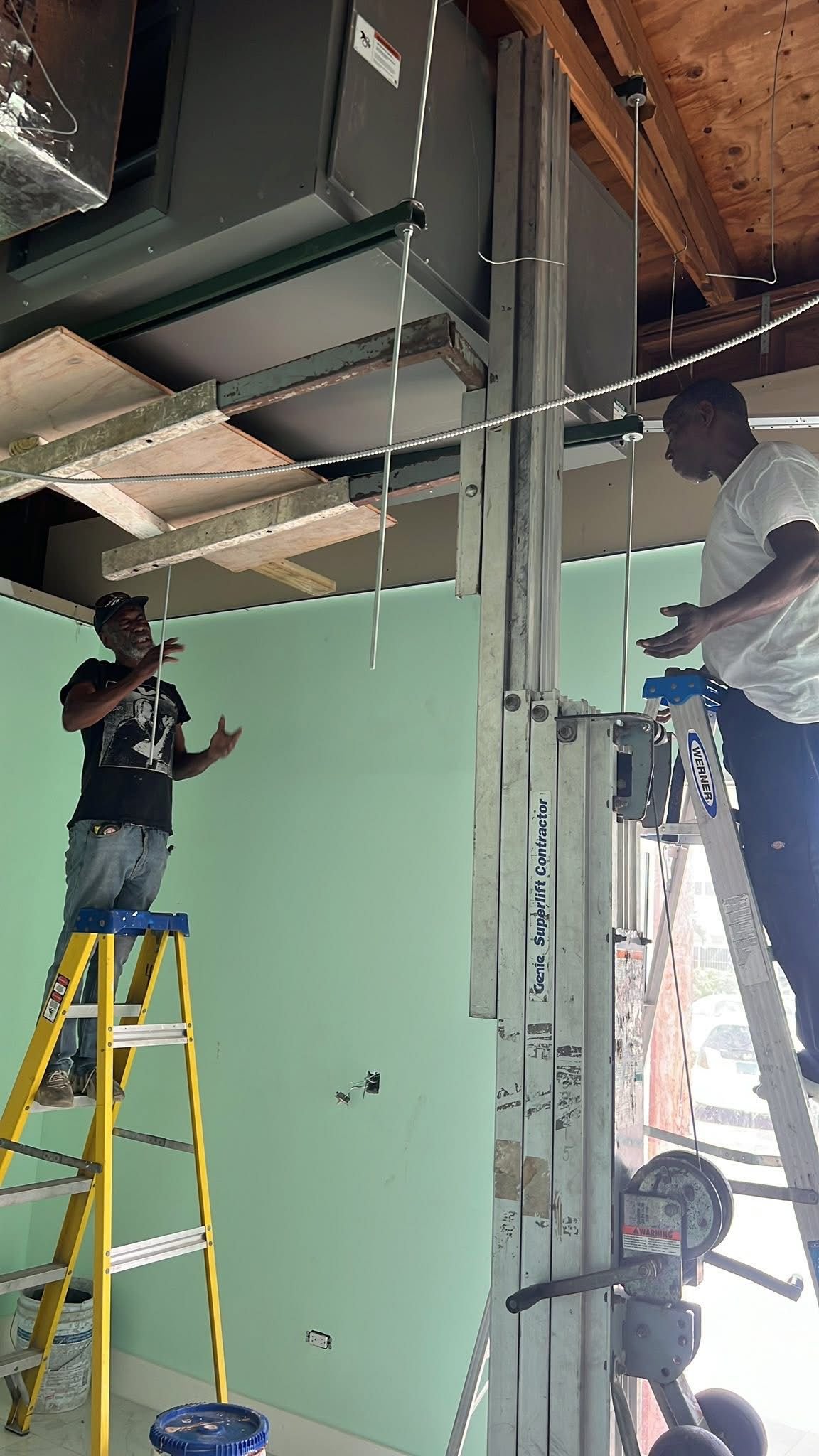 Two-man team installing large commercial HVAC unit with Genie Superlift